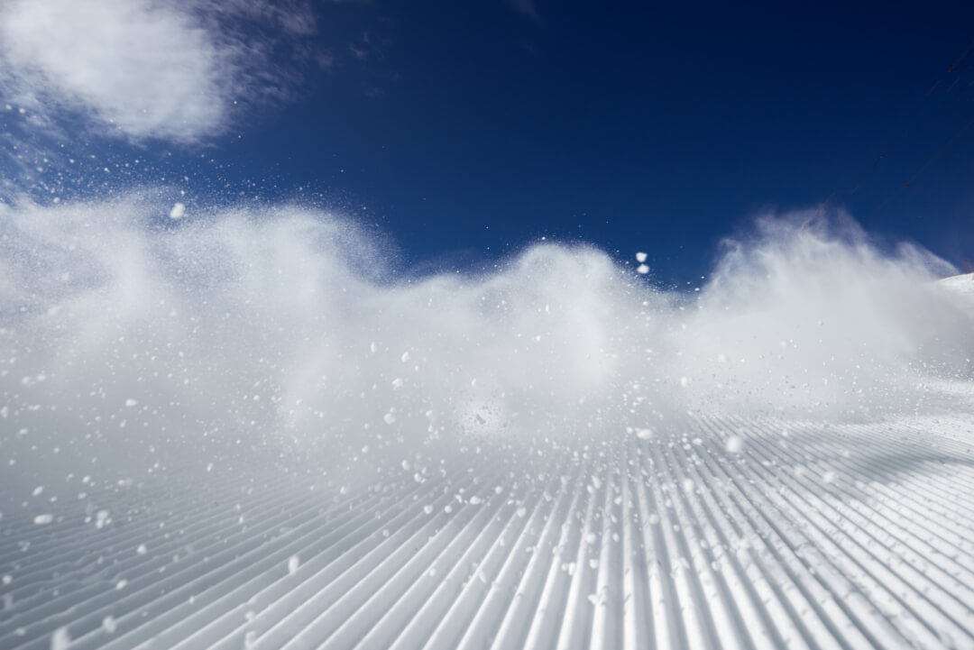 groomed snow at ski resort with snow spray, blue sky and cloud<br />
