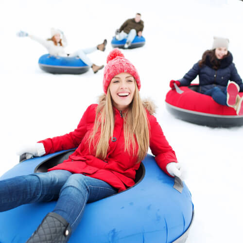 group of 4 friends tubing on snow with woman in red in front on blue tube
